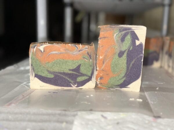 Two Pumpkin Spice rectangular bars of soap feature swirling patterns of orange, green, and purple on a white surface.