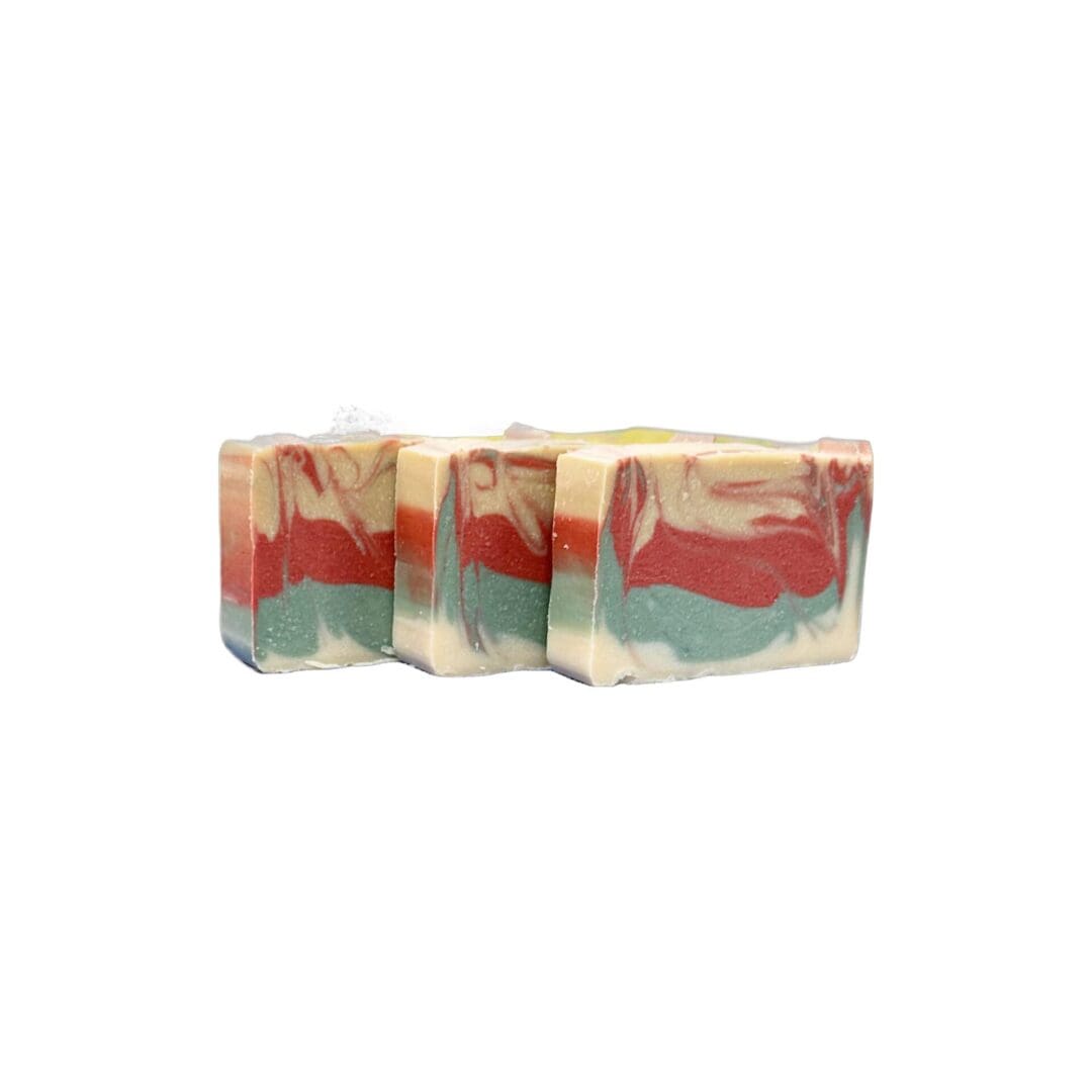 Three Winter Spruce bars of soap, showcasing colorful green, red, and cream layered patterns, are artfully arranged in a row against a plain white backdrop.
