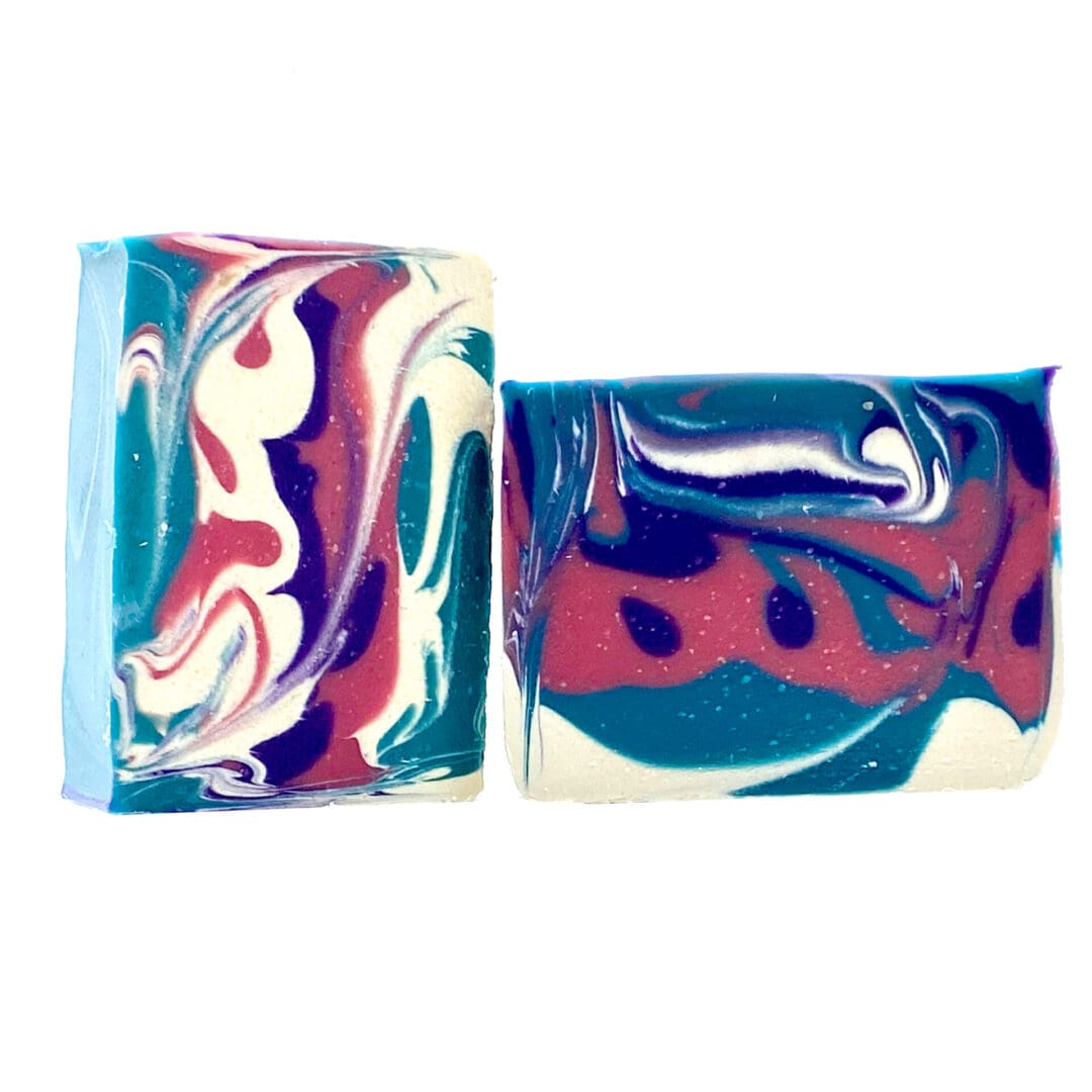 Two rectangular bars of Black Raspberry Vanilla soap feature swirling patterns in blue, pink, purple, and white, creating abstract designs on their smooth surfaces.