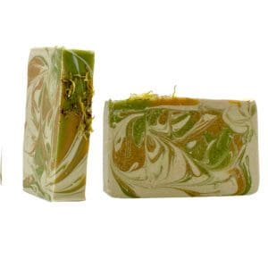 Two Cabin Fever artisan soap bars feature a swirled pattern of green, orange, and white. One bar stands upright adorned with dried herbs; the other lies flat.