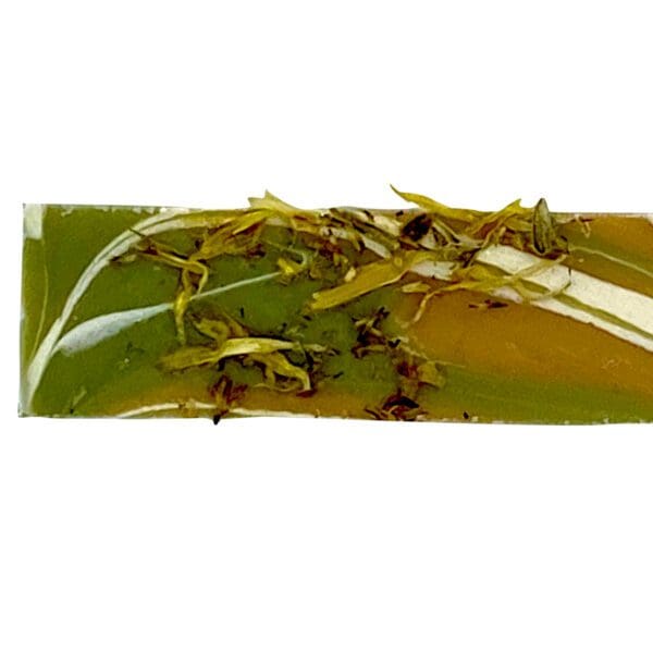 The Cabin Fever soap is a rectangular handmade bar featuring swirl patterns in green, white, and orange, with dried herbs embedded on its surface.