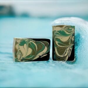 Two Glacial Tide bars, featuring swirls of green, black, and beige, rest bubbly on a wet surface.