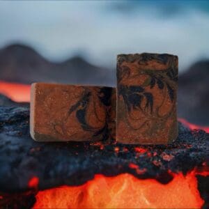 Two bars of Pahoehoe soap sit on a lava-like textured surface with a blurred mountainous backdrop.