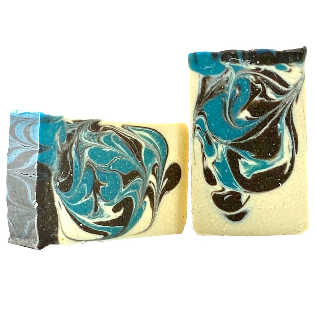 Two bars of Journey soap, featuring marbled black, blue, and white swirls, are positioned upright and leaning against each other.