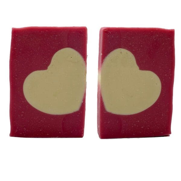 Two Love Spell soap bars, rectangular and pink with white heart shapes in the center, are placed side by side against a plain background.