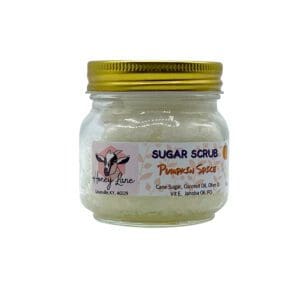 A small glass jar labeled "Pumpkin Spice Sugar Scrub" from Honey Lane, featuring a goat logo and ingredients such as cane sugar and coconut oil, with a gold metal lid.