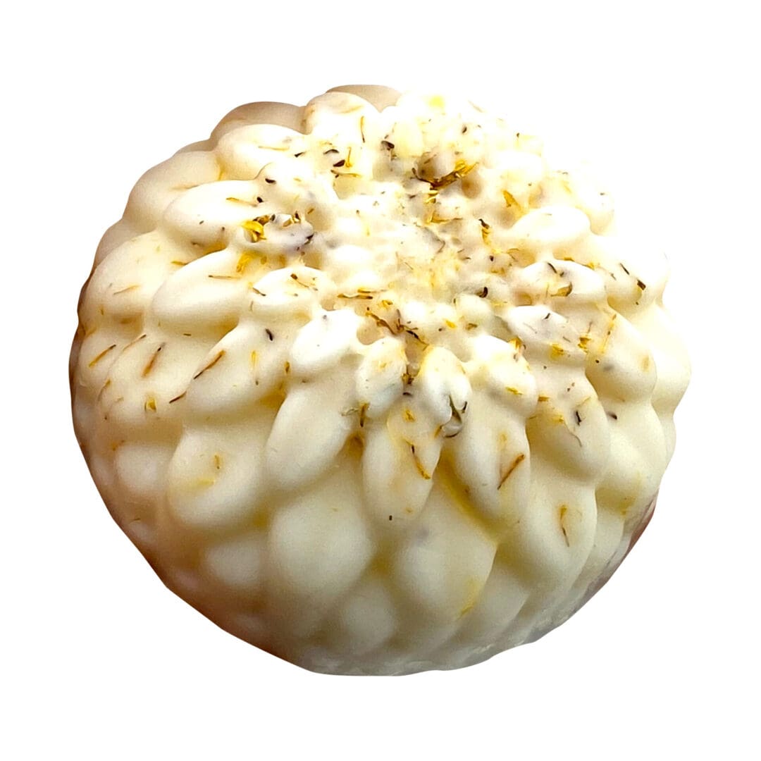 The Seventh Heaven Lotion Bar is a round, white, flower-shaped soap featuring small dried herb pieces on its surface, displayed against a white background.