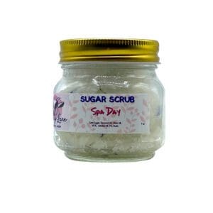 A small clear jar with a gold lid contains the "Spa Day Sugar Scrub," featuring ingredient and brand details on its label.