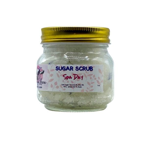 A small clear jar with a gold lid contains the "Spa Day Sugar Scrub," featuring ingredient and brand details on its label.